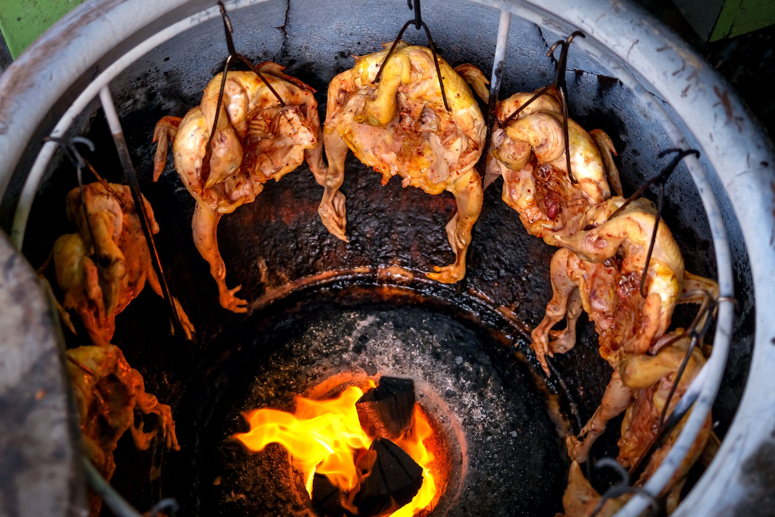 Juicy marinated chicken roasting evenly in a traditional tandoor oven over open flames.