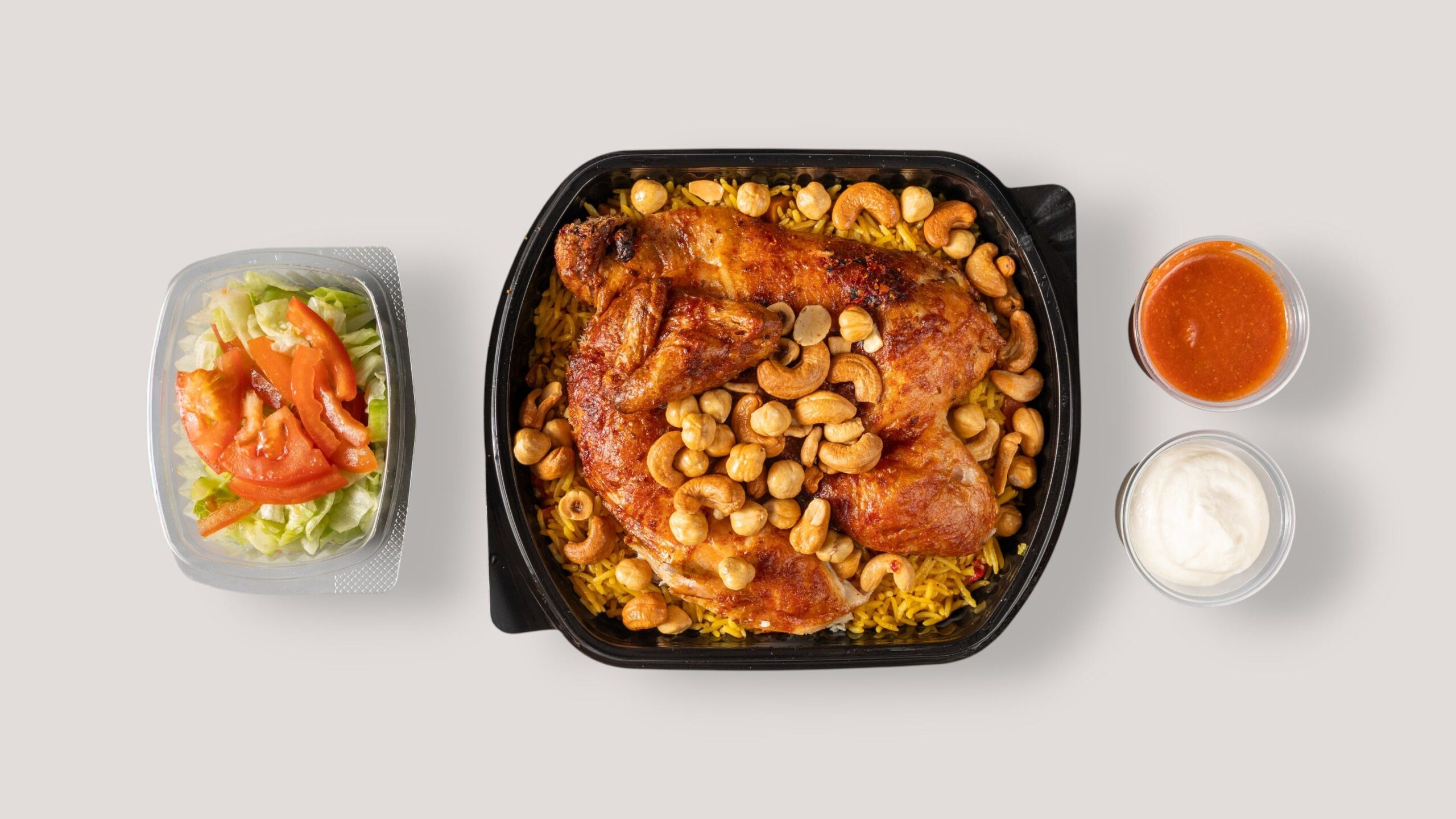 Top view of chicken biryani with cashews, salad, and sauces.